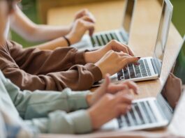 High school students sitting at the desk in the classroom during lesson, using laptops. Close up of hands, unrecognizable people.