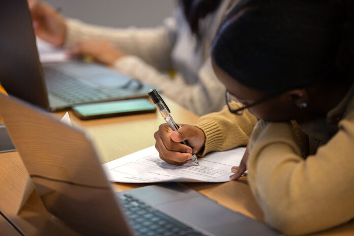 2025-08-CLAS_economics-writing-courses-ai.jpg A student focuses on completing a worksheet with a pen during class, with a laptop open in front of them.