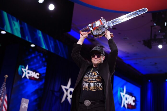 GettyImages-2200924488.jpg CEO of Tesla and SpaceX Elon Musk holding a chainsaw above his head.