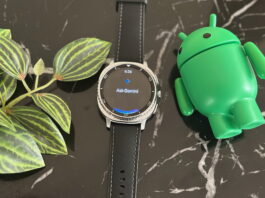 The Gemini app on the Samsung Galaxy Watch 8 Classic, which lays on a black marble table next to plant leaves and an Android mascot figurine.