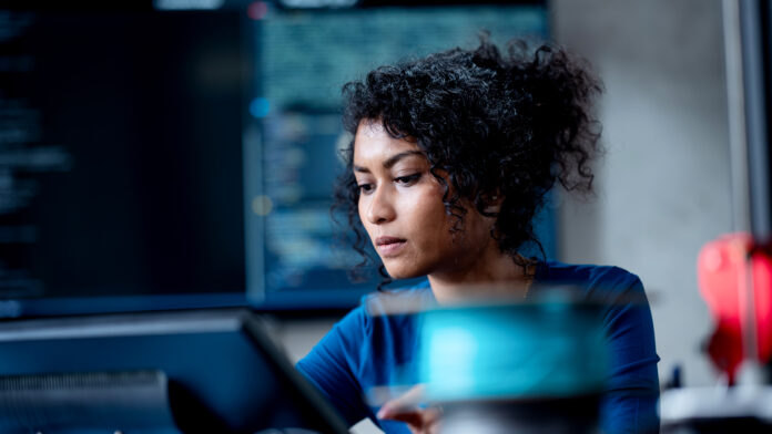 R6gCr8QcpbFXWcn6UnBkih.jpg Female software developer coding in Python programming language in an open place office space, with screen featuring code blurred in background.