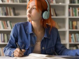 Student looking off into the distance wearing headphones while sitting at a desk with a laptop.