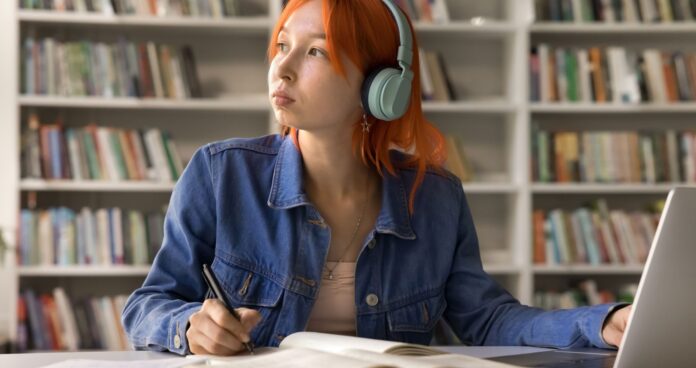 article-1.jpg Student looking off into the distance wearing headphones while sitting at a desk with a laptop.