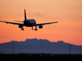 A passenger jet comes in for a landing, silhouetted against a dark pastel skyscape