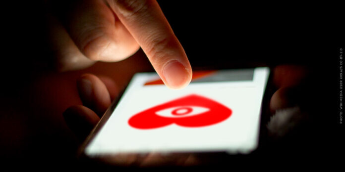 online-dating-1.jpg A person scrolls on a phone, viewing a spying heart