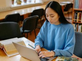 Young woman in blue long sleeve shirt sitting at a desk and typing on laptop computer