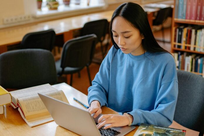 Young woman in blue long sleeve shirt sitting at a desk and typing on laptop computer