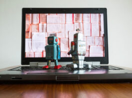 Two tin toy robots looking at laptop screen.