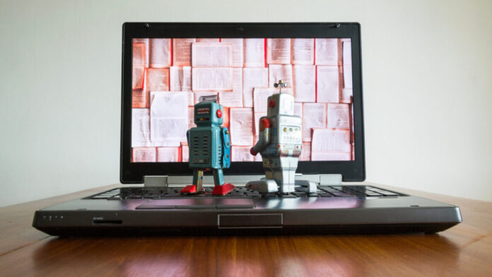 Two tin toy robots looking at laptop screen.