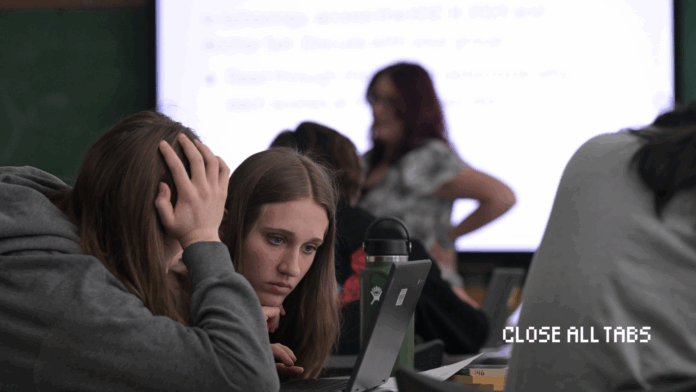 CAT-—-Teachers-Curbing-AI-Use-IMG.png Two female high school students hover over a computer. One student has a hand covering her face as the other student leans in closely to the computer screen.Their teacher and a projection of the lesson are blurred in the background. The Close All Tabs logo appears in pixelated font in the lower right corner.