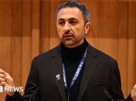 Suleyman dressed all in black, with an AI safety summit lanyard round his next, addresses the audience.