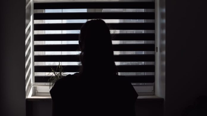 silhouette of girl sitting on bed in bedroom, rear view, daylight through Venetian curtain