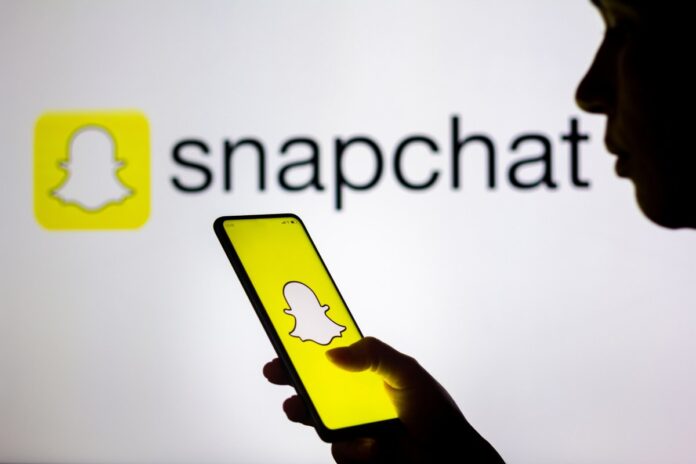 GettyImages-1239583734.jpg In this photo illustration, a woman's silhouette holds a smartphone with the Snapchat logo displayed on the screen and in the background.