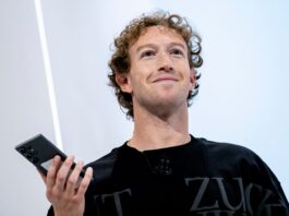 Mark Zuckerberg smiling while holding a phone on stage at an event