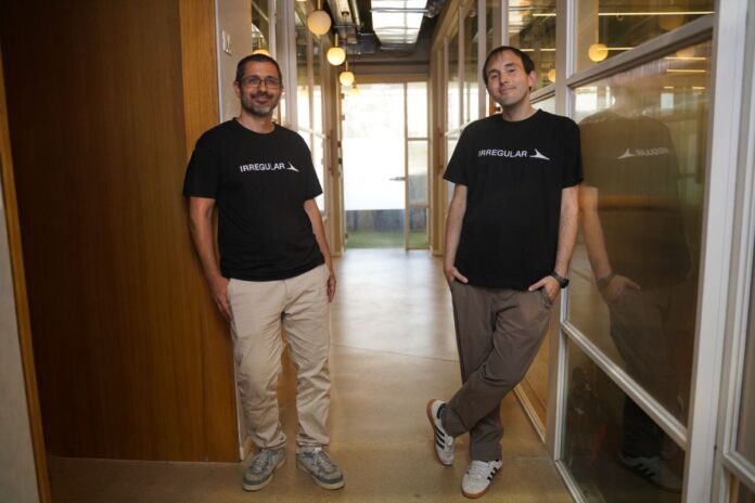 irregular-founders.jpeg The two co-founders stand abreast in an office hallway wearing black logo t-shirts.