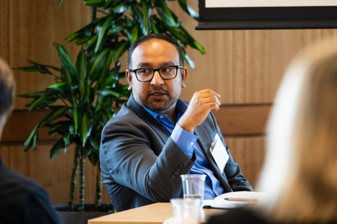 101525_AS_panel_001.jpg Doctor Abishek Murthy sitting at a table and gesturing toward two colleagues.