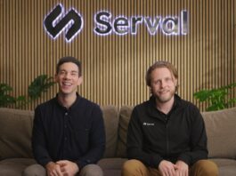 Two caucasian men sit on a couch with a company logo behind them.