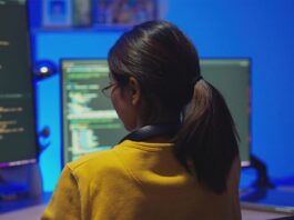 Female software developer coding in Python and JavaScript with code pictured on desktop computer screens in a home office.