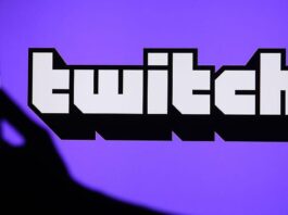 A hand holds a phone in front of the Twitch logo on a purple background.