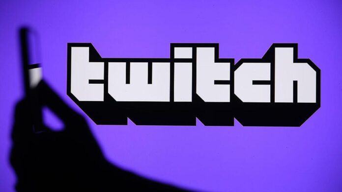 gettyimages-2236404173.jpg A hand holds a phone in front of the Twitch logo on a purple background.