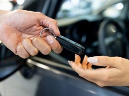 Woman sitting in a car and reaching her hand out to receive the keys from the salesperson at the dealership