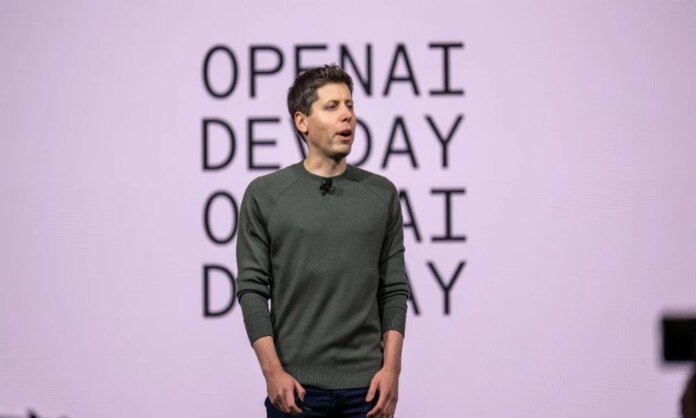 openai-devday-opening-keynote-1000x600.jpg An individual is standing on stage with "OPENAI DEMO DAY" in the background, wearing a dark green sweater and dark pants, presenting to an audience.