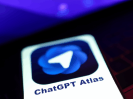 OpenAI Reveals Exciting New Features Coming to Its Atlas Browser A smartphone screen displaying the ChatGPT Atlas app icon, which features a white paper airplane symbol on a blue, swirling background. The phone is angled, with a blurred purple and dark background.