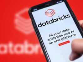 A photograph of a Databricks website on a phone being held in front of a larger, blurry version of the Databricks logo.