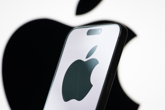 In this photo illustration, the logo of Apple Inc. is displayed on a smartphone screen, with the company's iconic black apple symbol visible in the background.