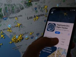 The Flightradar24 app is seen on a smartphone in front of a screen showing the live position of planes tracked by the app in the area of Los Angeles on August 5, 2022
