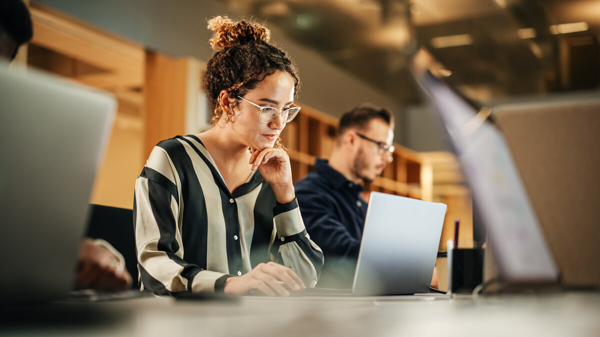 iStock-1481370371.jpg Portrait Of Enthusiastic Hispanic Young Woman Working On Computer In A Modern Bright Office. Confident Human Resources Agent Smiling Happily While Collaborating Online With Colleagues.