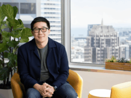 Airtable Unveils Superagent: Its Next-Generation AI Assistant A man in glasses and a dark blue jacket sits in a yellow chair in an office with a city view.