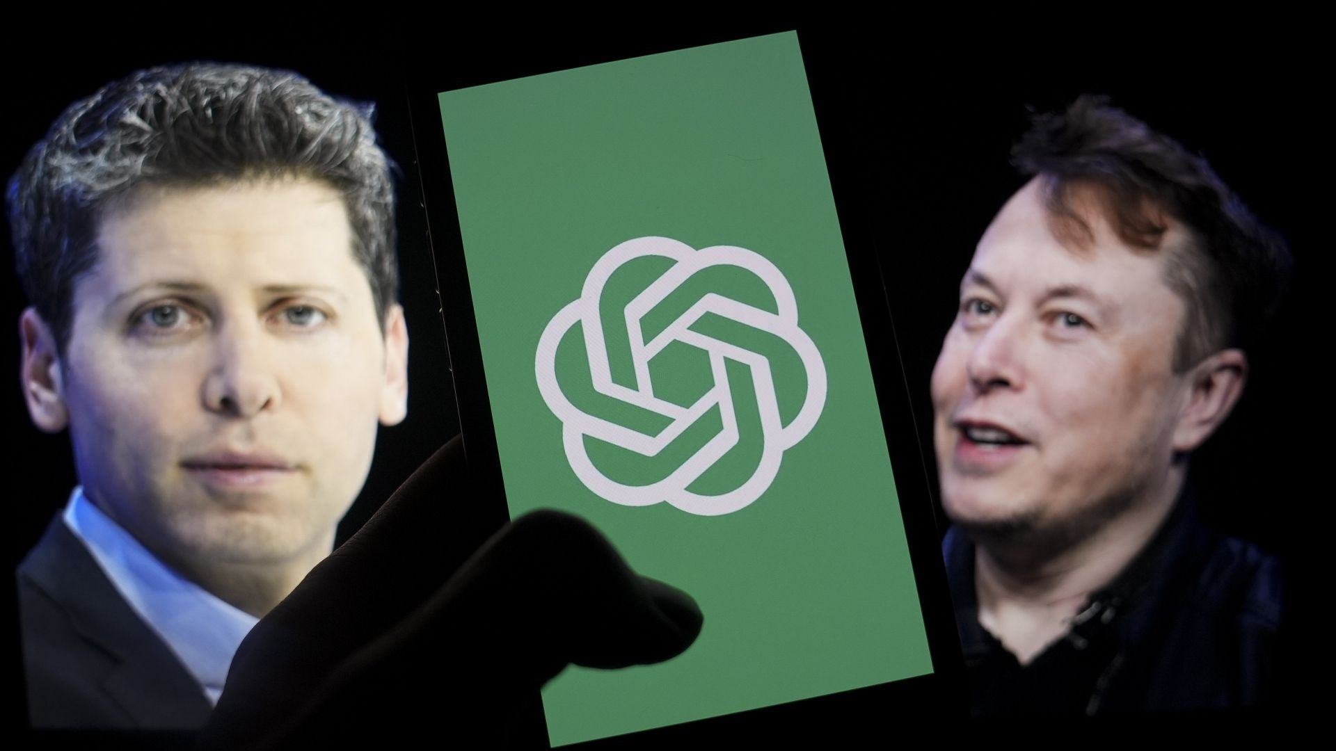 ehHTM977gYKf2ZpAopfCXB-1920-80.jpg The logo of 'OpenAI' is displayed on a mobile phone screen in front of a computer screen displaying the photographs of Elon Musk and Sam Altman.