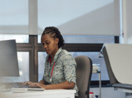 Side view shot of a female general practitioner sitting at her desk with a computer, typing on her keyboard.