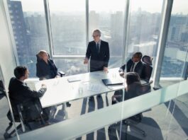 People talking in a conference room with tall windows overlooking a cityscape.