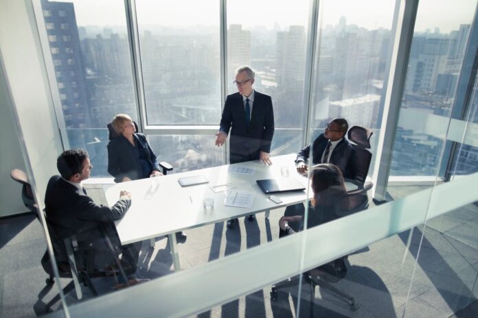 People talking in a conference room with tall windows overlooking a cityscape.