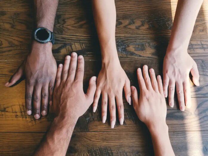 Five human hands on brown wooden table surface