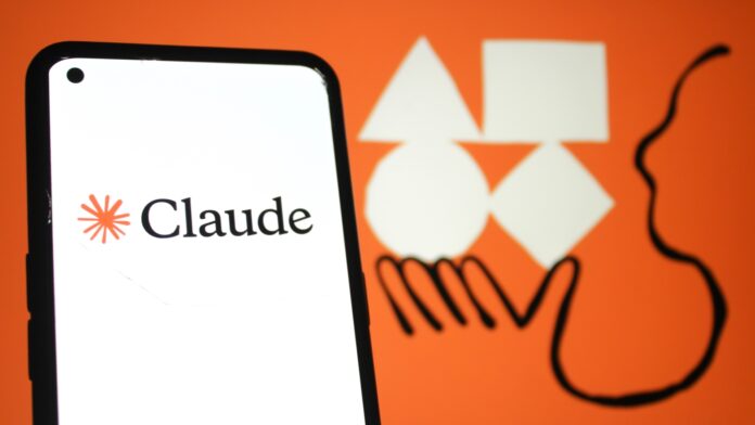 A close up of a smartphone displaying the Claude logo. Behind it, a large Claude artwork depicting a person's hand holding various shapes.