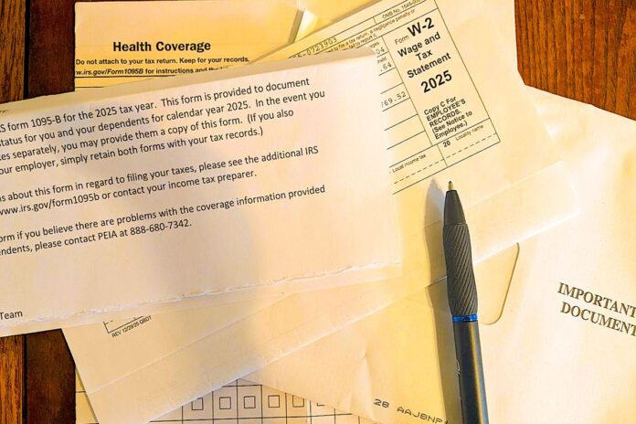 A stack of tax forms is shown on a table with a pen on top of the forms.