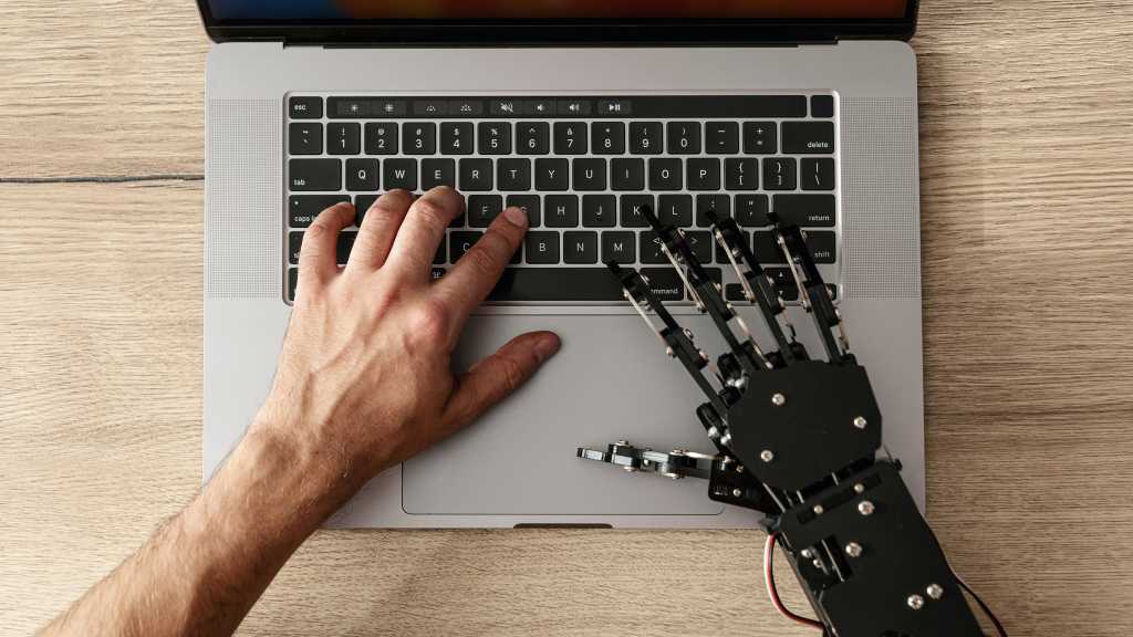 4148288-0-83269400-1774519486-AI-coding-assistant-shutterstock_2686070067.jpg image of a human and robot hand typing at a laptop