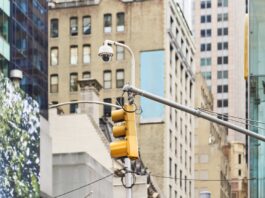 NYC Oversight Hearing Reveals Shortcomings in Agencies’ Utilization of AI and Surveillance Technology Security camera and traffic light are mounted on a pole, keeping watch over a bustling city street in New York City.