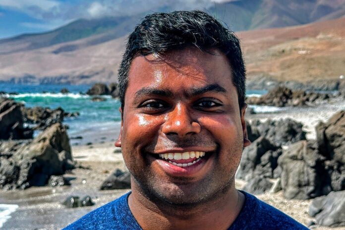 UCF computer engineering major Kamalakkannan Ravi smiles with the ocean and rocky shoreline blurred in the background.