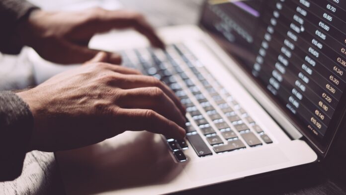Hands typing on a laptop keyboard with a spreadsheet visible on the screen.